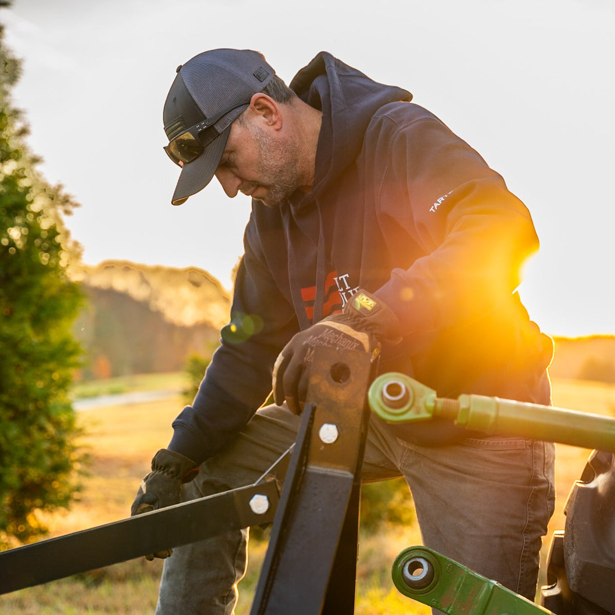 Man working on agricultural equipment in a field with sunset lighting